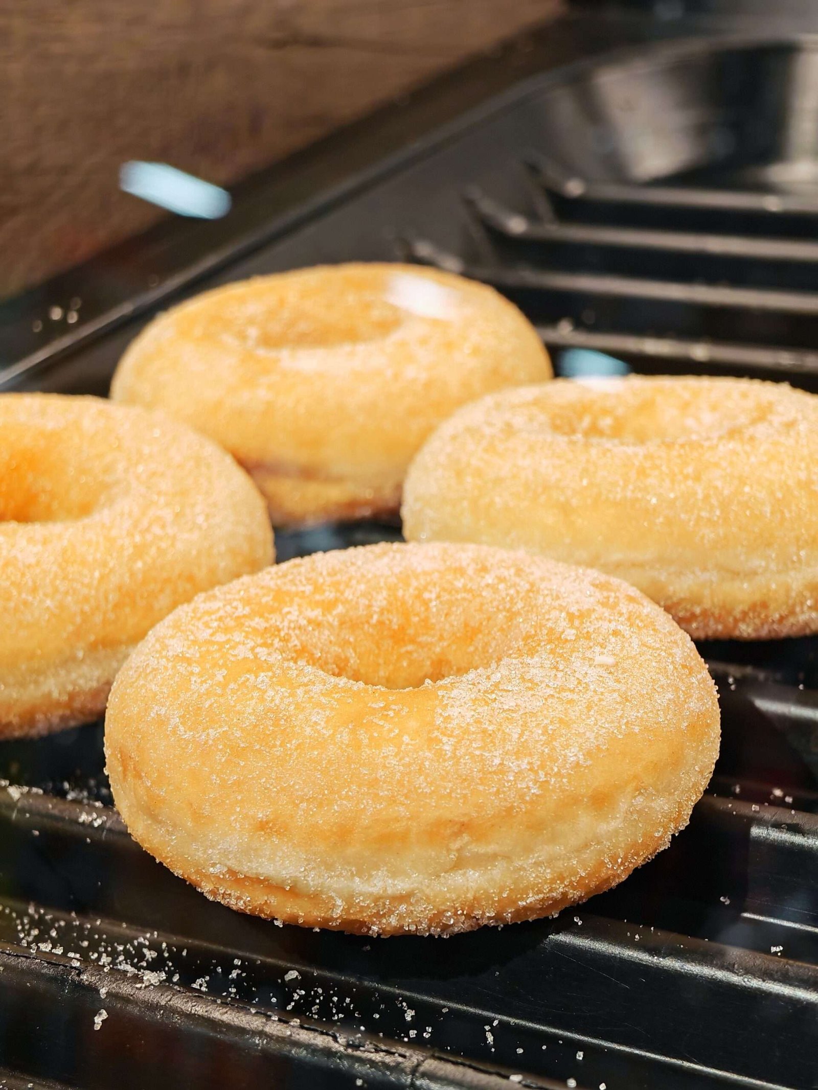 Close-up of four sugar-coated donuts resting on a griddle, freshly made.