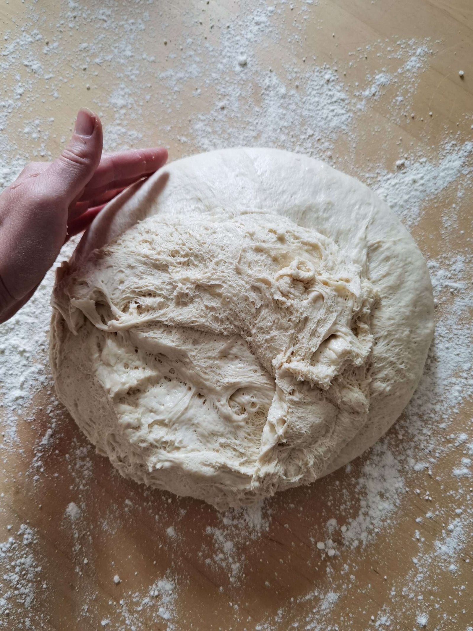 Close-up of a hand kneading fresh bread dough on a floured surface, perfect for baking themes.