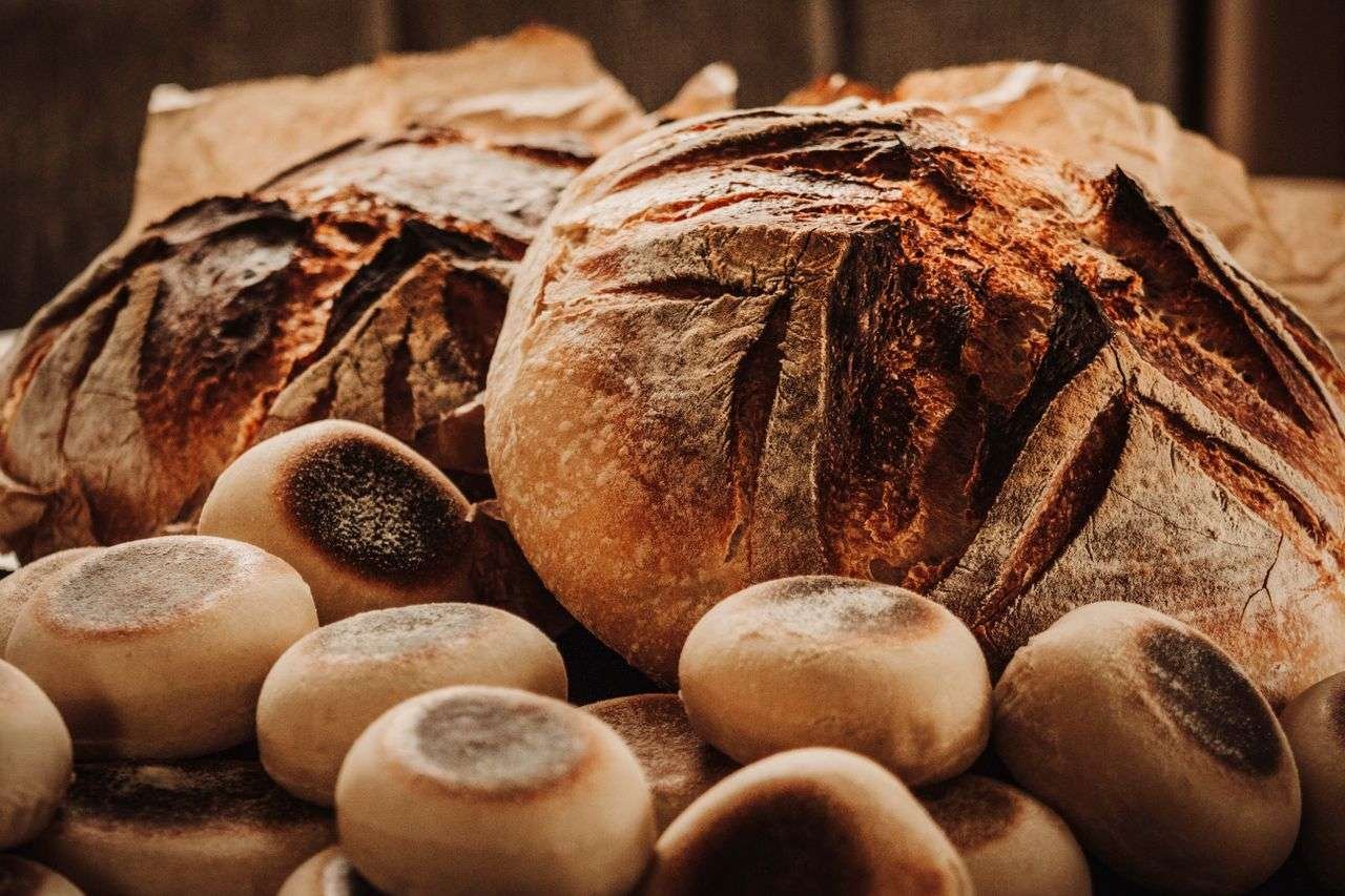 Close-up of freshly baked rustic sourdough loaves and buns in a warm, earthy setting.