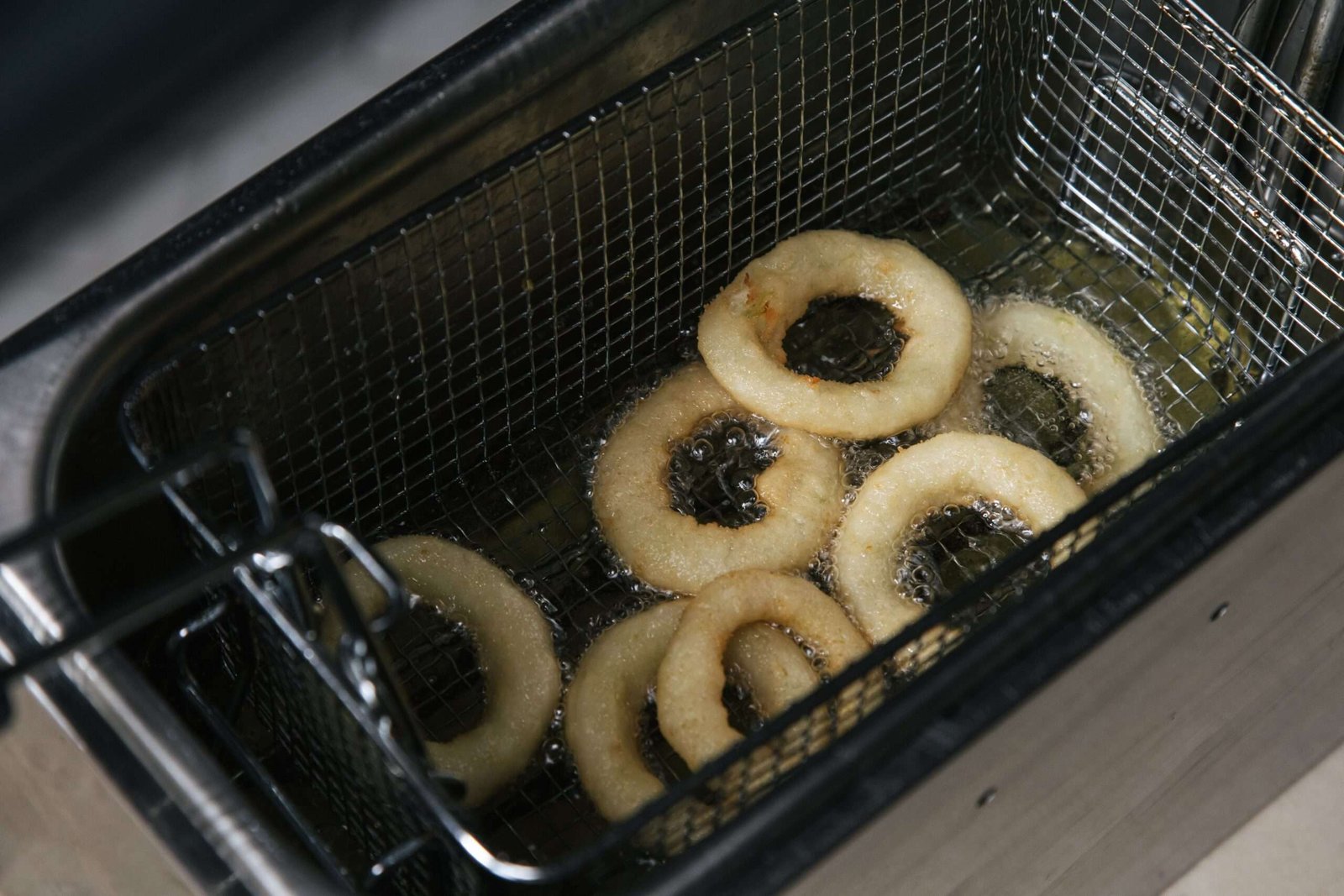 Hot crispy onion rings frying in oil in a deep fryer. Perfect food photography shot from above.